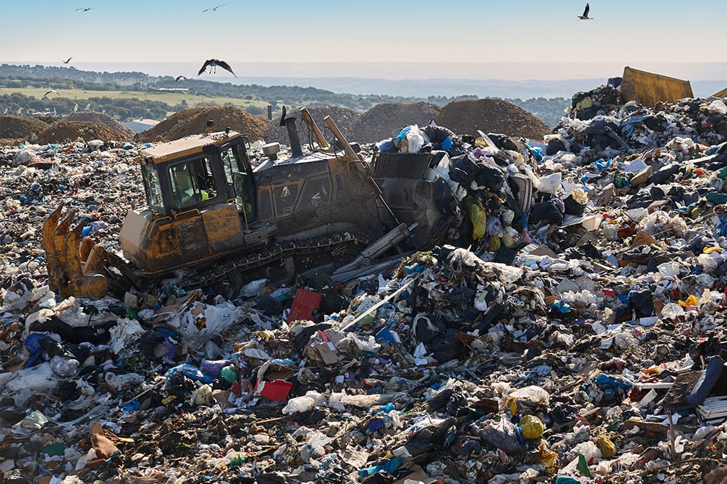 Bulldozer operating on a large landfill site surrounded by piles of waste