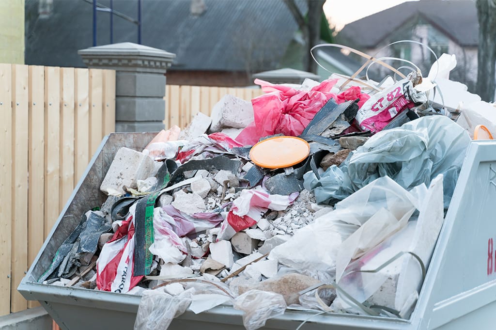 A full skip containing mixed construction waste, plastics, and rubble