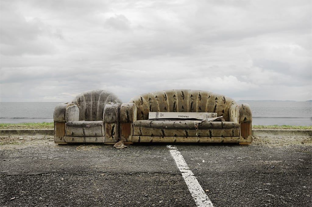 Worn-out sofa and armchair left outdoors near a road and waterfront